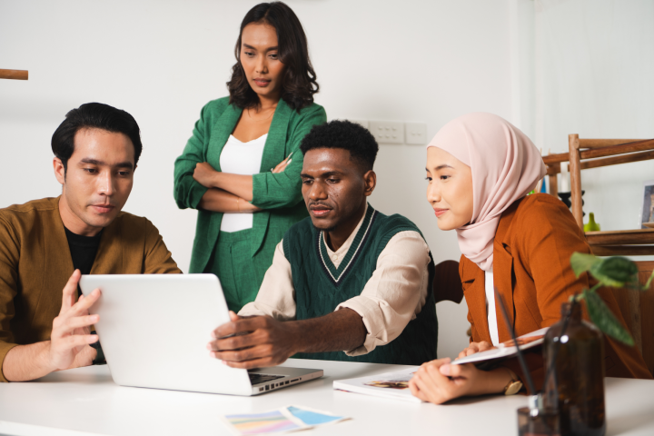 four students looking at a laptop and working together